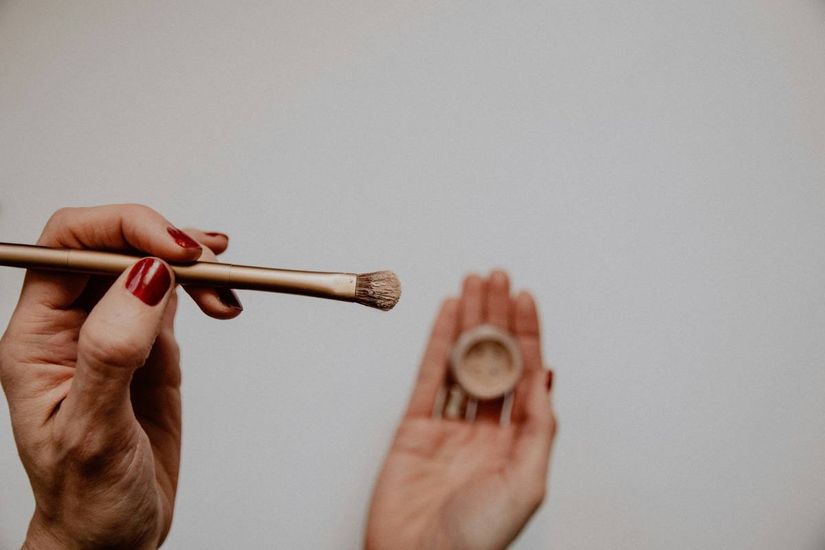 Close-up of a precision lip brush applying red liquid lipstick along the upper lip line with clean, sharp definition